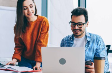 Ofiste dizüstü bilgisayar işbirliği ile çalışma yerine yakın pozitif gülümseyen erkek ve kadın, araştırma için kablosuz kullanarak samimi bir ortamda startup paylaşmak fikirleri üzerinde işbirliği erkek ve kadın çalışanlar