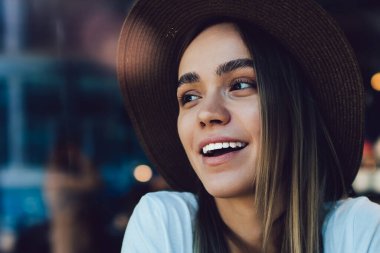 Keyifli ve neşeli genç bayan turuncu kitabı kucaklıyor ve kahvede pencerenin önünde otururken gülümsüyor ve başka tarafa bakıyor.