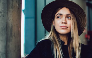 Şapkalı şık bir kadın, cep telefonu ve dizüstü bilgisayarla karanlık bir kafede rahat bir şekilde oturuyor.