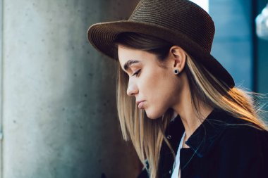 Kafe masasında dizüstü bilgisayarı ve kahveyle otururken panoda notları kontrol eden modaya uygun şapkalı ciddi genç bir kadının yan görüntüsü.