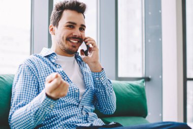 Mutlu gülümseyen erkek iletişim için arkadaşa arama ve rahat kanepede eğlence sırasında kapalı akıllı telefon konuşma yapmak için 4g kablosuz internet bağlantısı kullanarak toplantı için zaman tartışmak