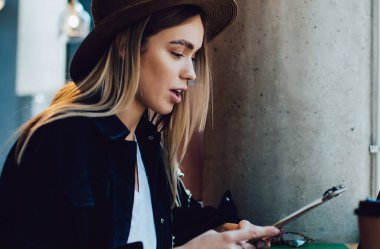 Kafe masasında dizüstü bilgisayar ve yemek fincanı ile otururken panoda notlar okuyan modaya uygun genç bayanın yan görüntüsü