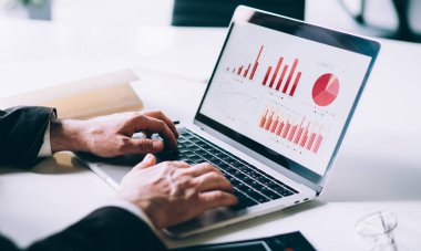Resmi kıyafet ve sakallı bir işadamı dizüstü bilgisayarını kullanarak şirketteki iş yerinin istatistiksel verileri üzerinde çalışıyor.