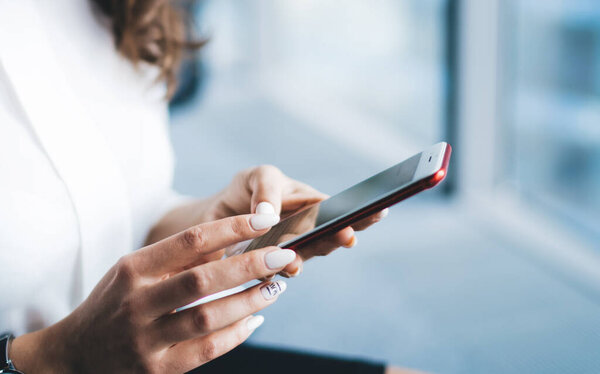 Обрезание улыбается красивая деловая леди в формальной одежде и наручные часы сидя серфинг смартфон на фоне синего размытости