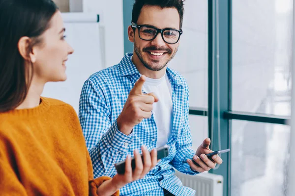 Akıllı telefon araçları üzerinden bilgi paylaşımı için kadın meslektaşı ile işten mola sırasında kameraya gülümserken optik gözlük işaret neşeli bin yıllık hipster adam Portresi