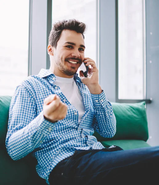 Mutlu gülümseyen erkek iletişim için arkadaşa arama ve rahat kanepede eğlence sırasında kapalı akıllı telefon konuşma yapmak için 4g kablosuz internet bağlantısı kullanarak toplantı için zaman tartışmak