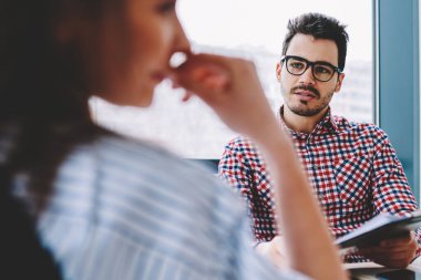 Görme düzeltme için optik gözlük akıllı genç erkek girişimci seçici odak kadın ortağı ile ofis masaüstünde oturan ve klasörden analiz için bilgi tartışıyor