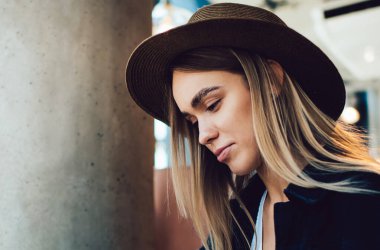 Kafe masasında dizüstü bilgisayar ve kırtasiyeyle oturup ders çalışırken şapkalı genç bir kadının not alırken yan görüntüsü.