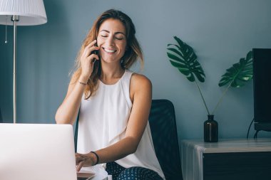Beyaz kadın evde dinleniyor. En iyi arkadaşıyla yaptığı akıllı telefon konuşmasında seviniyor. Mutlu gülümseyen hippi kız dizüstü bilgisayarda oturuyor ve cep telefonuyla konuşuyor.