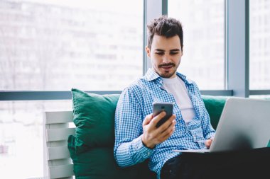 Pozitif hipster adam cep telefonu ve dizüstü bilgisayar cihazı ile bluetooth bağlantısı kullanarak uzaktan kapalı çalışırken bilgi paylaşımı, beyaz erkek cep telefonu uygulaması üzerinden gelen mesajı okuma
