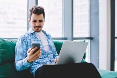 Pozitif hipster adam cep telefonu ve dizüstü bilgisayar cihazı ile bluetooth bağlantısı kullanarak uzaktan kapalı çalışırken bilgi paylaşımı, beyaz erkek cep telefonu uygulaması üzerinden gelen mesajı okuma