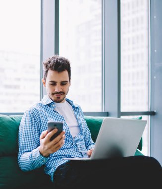 Pozitif hipster adam cep telefonu ve dizüstü bilgisayar cihazı ile bluetooth bağlantısı kullanarak uzaktan kapalı çalışırken bilgi paylaşımı, beyaz erkek cep telefonu uygulaması üzerinden gelen mesajı okuma