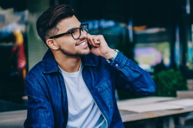 Gözlüklü neşeli beyaz erkek, dışarıda oturan cep telefonu sohbeti yapan, trendy giyimli mutlu hipster adam telefon görüşmesi yaparak dolaşımdaki bağlantıdan memnun ve gülümseyen
