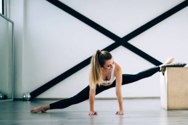 Çağdaş spor salonundaki siyah spor duvar dirençli bantlara karşı tahta blok kullanarak aktif giyimde konsantrasyon ve bacak esnetme konusunda kararlı bir sporcu.