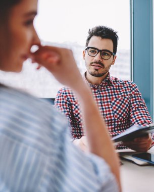 Görme düzeltme için optik gözlük akıllı genç erkek girişimci seçici odak kadın ortağı ile ofis masaüstünde oturan ve klasörden analiz için bilgi tartışıyor