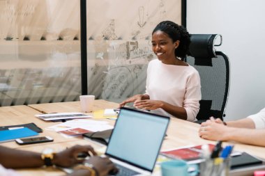 Modern ofis odasındaki iş arkadaşlarıyla kooperatif proje üzerinde çalışan Afro-Amerikan neşeli genç bayan.