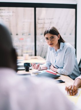 Ciddi genç iş kadını, yönetim kurulunda toplanırken, çeşitli meslekdaşlarına girişim projesi ve kurumsal anlaşma hakkında ısrarla fikir beyan ediyor.