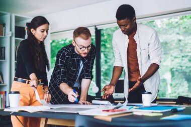 Düşük açılı düşünceli çeşitli çalışanlar tartışırken yeni bir proje yaratıyorlar. Çağdaş ofiste kağıtlarla masaya oturuyorlar ve sıcak içecekleri götürüyorlar.