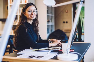 Modern netbook ile birlikte çalışan şık optik gözlüklü akıllı kadın grafik tasarımcısı, serbest çalışma için modern netbook, kameraya gülümseyen beyaz kadın blog yazarı portresi