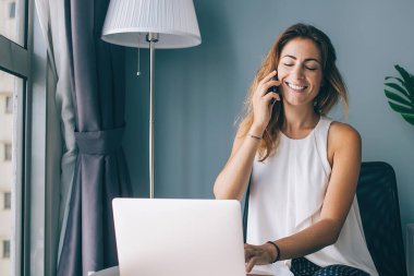 Beyaz kadın evde dinleniyor. En iyi arkadaşıyla yaptığı akıllı telefon konuşmasında seviniyor. Mutlu gülümseyen hippi kız dizüstü bilgisayarda oturuyor ve cep telefonuyla konuşuyor.