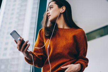 Cep telefonu, kulaklık düşünceli kadın uzağa bakarak uygulama üzerinden favori müzik çalma listesi dinlerken romantik şarkı kelimeler üzerinde düşünme düşünceli kadın meloman duygu