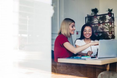 İş yerinde gülümseyen etnik meslektaşımla birlikte üzerinde çalıştığımız projenin ekranını gösteren günlük kıyafetlerle mutlu serbest çalışanların penceresinden bakın.