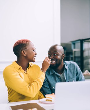 Neşeli, gülümseyen Afro-Amerikan çift kahve dükkanında kahve ve dizüstü bilgisayarla masada oturmuş tatlı ve kek yiyorlar.