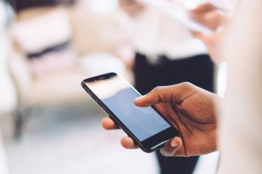 Meçhul etnik çalışanların elleri bulanık arka planda meslektaşlarıyla ofiste dururken modern akıllı telefonlara göz atıyorlar.