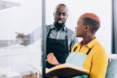Ciddi Afrikalı Amerikalı küçük işletme sahiplerinin düşük açılı tartışmaları ve muhasebe yaparken vitrinin yanında durup ürünlerin ulaşılabilirliğini kontrol etmesi ve fiyatların analiz edilmesi