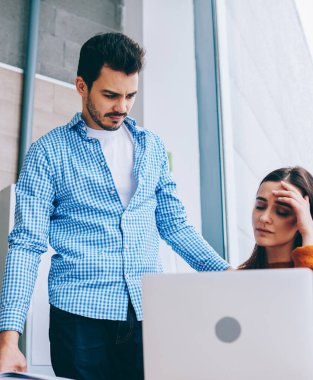 Hayal kırıklığına üzgün kadın ofis çalışanı dizüstü bilgisayar ile masaüstünde oturan son tarihten yorgun hissediyorum bakmak. Erkek yönetici, düşük üretkenlikten şikayet eden kadın sekreterin yanında duruyor. Basınç