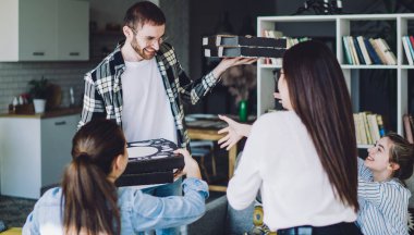 Keyifli bir adam, rahat bir oturma odasında parti yaparken, eve servis pizzalarıyla dolu karton kutular veriyor.