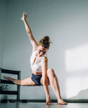 Esnek kadın plie pozisyonunda geriliyor. Sağ bacağı barre ve el kaldırıyor. Gündüz vakti parlak stüdyoda.