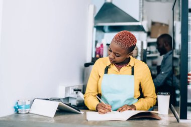 Özenli Afro-Amerikan muhasebe muhasebe, modern kantinde yiyecek ürünlerinin olduğu vitrinin yanında hazır sıcak içecekle tezgahta dururken.