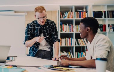 Modern ofiste proje tartışması sırasında masanın yanında dururken gülen çoklu etnik gruptan iş arkadaşlarıyla konuşan iyimser genç adam.
