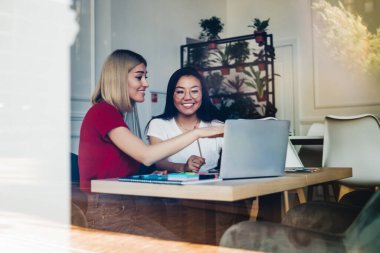 İş yerinde gülümseyen etnik meslektaşımla birlikte üzerinde çalıştığımız projenin ekranını gösteren günlük kıyafetlerle mutlu serbest çalışanların penceresinden bakın.