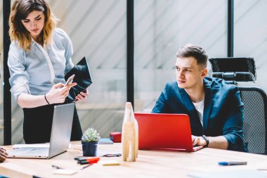 Çalışanlara akıllı telefonda dijital bilgi gösteren konsantre kadın yönetici, genç iş arkadaşlarının sosyal ağda haber okurken ofis iç mekanlarında bir arada oturarak masada oturuyor