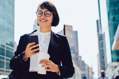Finans bölgesinde kentsel ortamda iş molası sırasında akıllı telefon uygulaması üzerinden online iletişim kurmak için modern teknolojiyi kullanarak zarif takım elbiseli gülümseyen şirket yöneticisinin yarım uzunlukta portresi