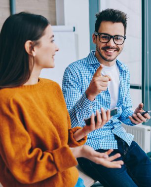Akıllı telefon araçları üzerinden bilgi paylaşımı için kadın meslektaşı ile işten mola sırasında kameraya gülümserken optik gözlük işaret neşeli bin yıllık hipster adam Portresi