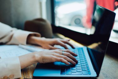 Modern şehir kafesinde masa başında uzaktan çalışırken bej rengi gayri resmi takım elbiseli kadın klavyede daktilo kullanıyor.