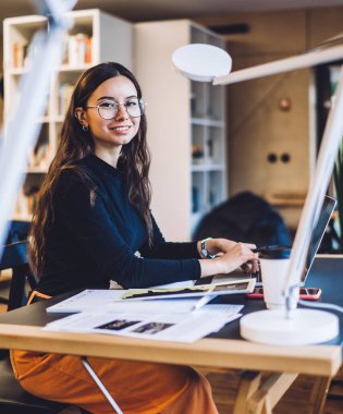 Modern netbook ile birlikte çalışan şık optik gözlüklü akıllı kadın grafik tasarımcısı, serbest çalışma için modern netbook, kameraya gülümseyen beyaz kadın blog yazarı portresi