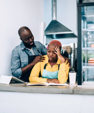 Afrikalı Amerikalı erkeği önemsemek omuzlara dokunmak ve üzgün kadını teselli etmek, muhasebe ve iş ile ilgili sorunlar yaşarken aynı zamanda açık modern pastanede ayakta duruyor.