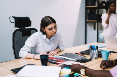 Erkek işçi, öğleden sonra ofisteki cep telefonuyla konuşurken kadın meslektaşına belge gösteriyor ve fikirlerini dile getiriyor.