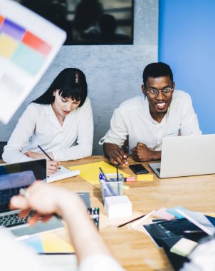 Modern erkek ve kadın işçiler istatistik kağıtları ve cihazlarla masada toplanıp şirkette iş planlarını tartışıyorlar.