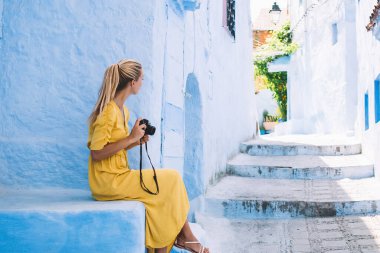 Rastgele bacak bacak üstüne atmış, Fas 'ta taş merdivenlerde oturan kamera kullanan sarışının yan görüntüsü