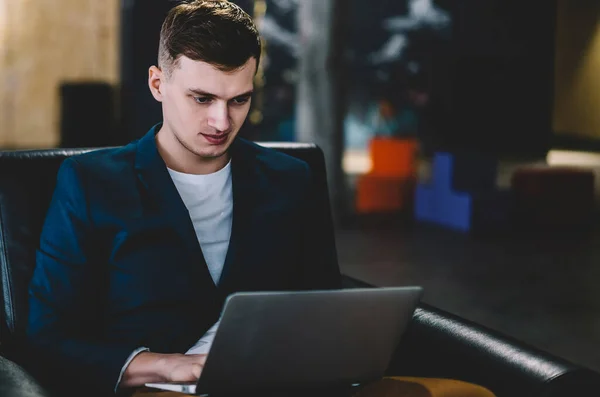 Serious caucasian male programmer creating new website via application on laptop device, young man using wireless 4g connection on computer for making research of information for startup project