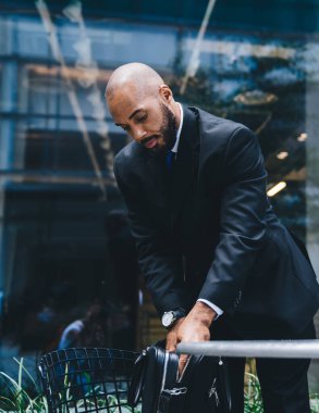 Seçkin yönetici, takım elbiseli kel adam, ticari binanın önünde siyah deri evrak çantasını açıyor.