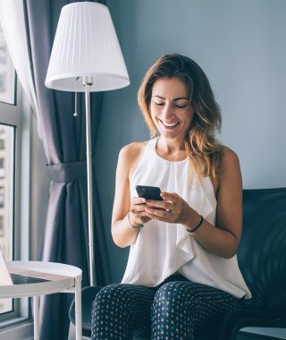 Beyaz kolsuz bluzlu, mutlu, genç, esmer kadın. Yuvarlak masada oturuyor. Akıllı telefonuyla mesaj yazıyor.