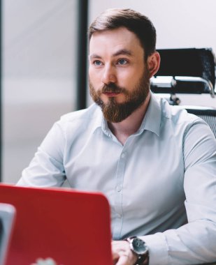 Ofis masaüstü önünde oturan meslektaşından sakallı ciddi erkek grafik tasarımcı dinleme bilgileri, çalışanları ile işbirliği sırasında dizüstü bilgisayar üzerinde çalışan genç adam. Yetişkin erkek işçi