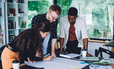 Resmi giysiler içindeki düşünceli farklı çalışanların yüksek açısı kağıt üzerinde bilgileri kontrol ederken, yeni projeyi belgelerle birlikte masanın üzerinde duruyor.