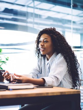 Neşeli bir Afrikalı Amerikalı çift, modern kafenin penceresinin yanındaki ahşap masada otururken sohbet ediyorlar.
